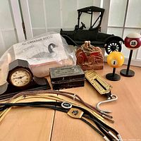 Wide view of lot including black metal model car decor, pool ball desk decor with numbers 1 and 15, Merrie Olds ceramic container (firetruck shaped), old metal box, pocket balance scale, bolo ties, and mantel clock.