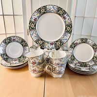 Wide view of all dishes including stacked plates, saucers, and teacups showing the pattern and quantity in the set