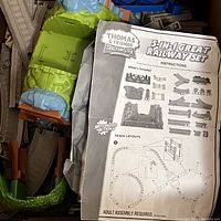 Photo showing folded instruction manual for Thomas & Friends TrackMaster 5-in-1 Great Railway Set on top of assorted green, brown, and gray plastic track parts and accessories.