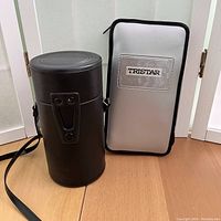 Black leather cylindrical lens case with shoulder strap and buckle closure next to a silver zippered folder with Tristar logo.