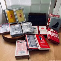 Photo shows all ten vintage advertising playing card decks arranged on a table showing partial box designs and colors.