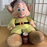 Front view of the large Dopey plush seated beside a can of Dr Pepper for scale, showing the size and condition of the plush.