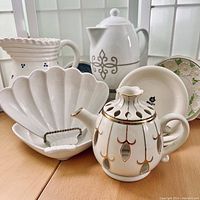 Front view of all items showing white ceramic vessels and plates with gold and floral details