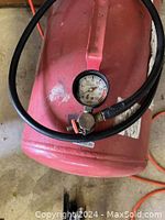 Photo showing close-up view of red air tank with pressure gauge and black hose wrapped around it, highlighting paint wear and scuffs.
