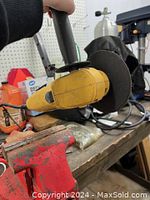Angle grinder held at an angle showcasing the yellow body, black side handle, and part of the cutting disc edge.