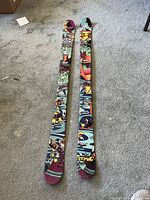 Two Atomic skis lying flat on carpet, top side with graphic design visible.