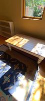 Photo showing a white wooden coffee table in natural light beside a window, placed on a patterned rug.