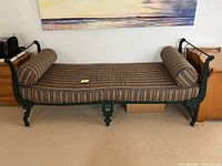 Full front view of the green wrought iron day bed with striped cushion and two cylindrical bolsters on each end.