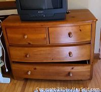 Wooden dresser with four drawers, showing worn condition and one drawer hanging unevenly but closing flush. TV placed on top for size reference.