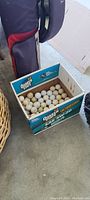 Photo of a box containing many used white golf balls labeled Quaker State SAE 5W-20.