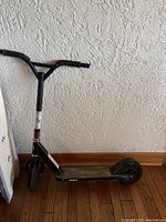 Side view of used black Razor scooter leaning against wall showing overall condition and design