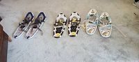 Three pairs of snowshoes laid out on carpet showing different styles and bindings