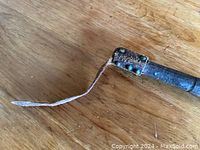 Close-up of the leather strap at the end of the hammer’s wooden handle on a wooden surface.