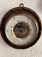 Front view of aneroid barometer weather vane showing detailed face with weather and pressure indicators and central mechanism under glass.