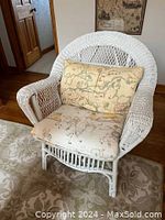 Full view of white wicker armchair with map-patterned cushions in room setting.