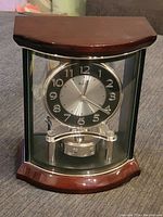 Full front view of the Bulova clock showing curved wood top and base with glass panels enclosing the clock face and pendulum.
