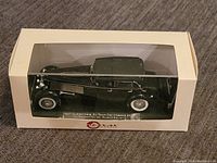 Front view of the black 1937 Duesenberg SJ Town Car model inside white display box showing clear plastic window.