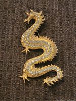 Front view of gold-tone dragon brooch adorned with clear rhinestones, showing detailed textured design and facial features.