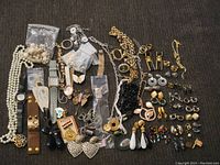 Wide view of entire jewelry lot showing watches, necklaces, earrings, brooches, and pins arranged on a surface.