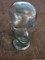 Front and side view of a clear glass head sculpture showing facial features and base.