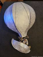 Front view of large tin hot air balloon model showing balloon, basket hanging below, and figurines inside.