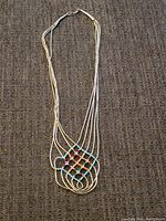 Full view of the liquid silver multiple strand necklace with colorful beaded pendant on a brown fabric surface.