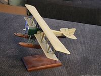 Side angle view of the vintage biplane model airplane mounted on a wooden stand, showing details of the wings, floats, and rigging wires.