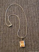 Full view of a sterling silver necklace with a rectangular pendant featuring an amber-colored stone.