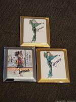 All three Lorraine compacts, showing detailed artwork on enamel panels with gold and silver borders on a dark carpet background.