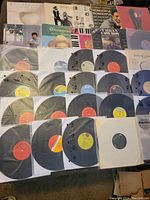 Photo shows a broad assortment of vinyl records laid out, some in original covers including St. Vincent and Christmas With The Jets, others in generic or white paper sleeves. Labels vary in color and text.