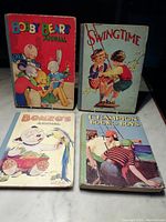 Four 1940's children's annual books with illustrated colorful covers stacked on a tabletop.