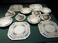 Complete set of four place settings displayed, showing plates, bowls, cups, and saucers with embossed floral design in purple, yellow and green hues.