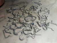 Several chrome-finished, metal pegboard hooks of different styles and sizes spread out on a marble surface.