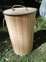 Full view of the bamboo hamper standing upright outside, showing the tapered cylindrical shape and side handles.