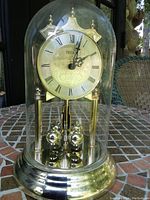 Full view of the gold anniversary clock with glass dome on a tiled table, showing its overall appearance and structure.