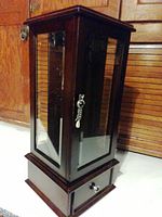 Full view of the jewelry display case showing front and side with metal knob drawer and glass panels.