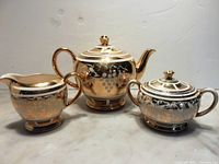 Front view of Sadler teapot, creamer, and sugar bowl showing gold grapevine pattern on ivory ceramic