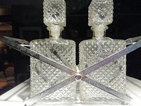 Two square diamond cut glass decanters with stoppers, secured in a metal caddy holder with crossed bars.
