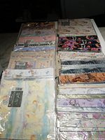 Photo showing multiple stacks of unopened wrapping paper packages with various patterns including pastel cartoon angels, baby announcements, cats, and floral prints.
