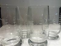 Four clear bar glasses with etched sailing ship designs, arranged in a row, displayed on a white surface.