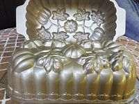 Close-up of two cast aluminum pumpkin loaf pans showing the detailed pumpkin and leaf decoration and the gold finish.
