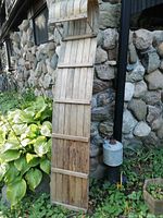 Full length view of the wooden toboggan showing its narrow design, wooden slats, and overall condition against a stone wall background.