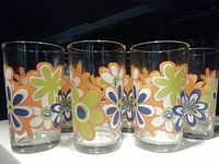 Front view of multiple glasses showing colorful flower designs in orange, green, navy blue, and white on clear glass