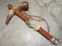 Full length top view of the ceremonial rattle showing the horn shape, leather wrapping, feathers, and bead detail on leather thong.