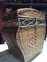 Side view of a wicker storage hamper showing the woven basket, metal frame, and caster wheels.