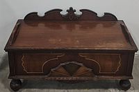 Closed view of the ornate wooden antique blanket chest showing carved details and a scalloped top edge with floral motif.