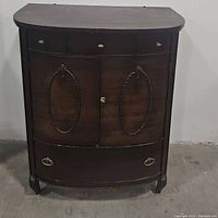 Front view of antique wooden cabinet showing three top drawers, two decorated front doors, and one large bottom drawer.