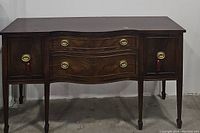 Front view of antique mahogany sideboard showing drawers and cabinet doors closed, highlighting brass hardware and wood grain.