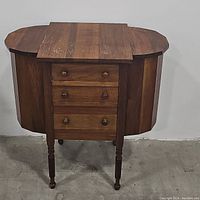 Front view of the antique sewing cabinet with side panels folded down and three closed drawers visible.