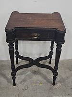 Full view of the antique wooden side table showing top, legs, drawer with brass pull, and base stretcher.